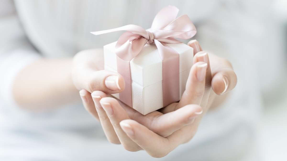 Close up: a female escort holds a white gift box wrapped with pink ribbon.