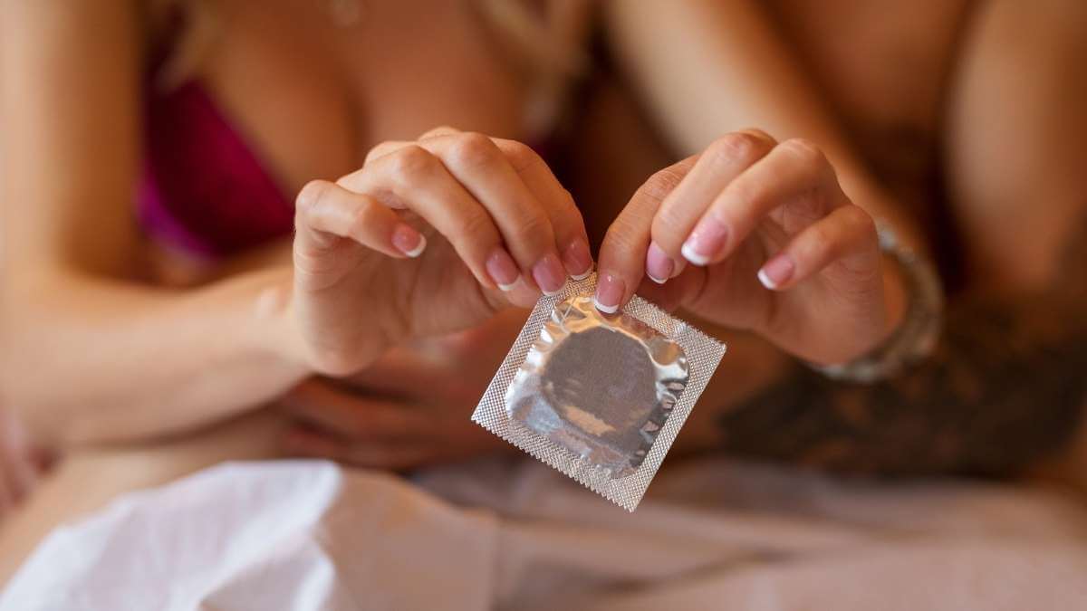 Close-up: A Melbourne escort with pink nails opens a condom packet in bed.