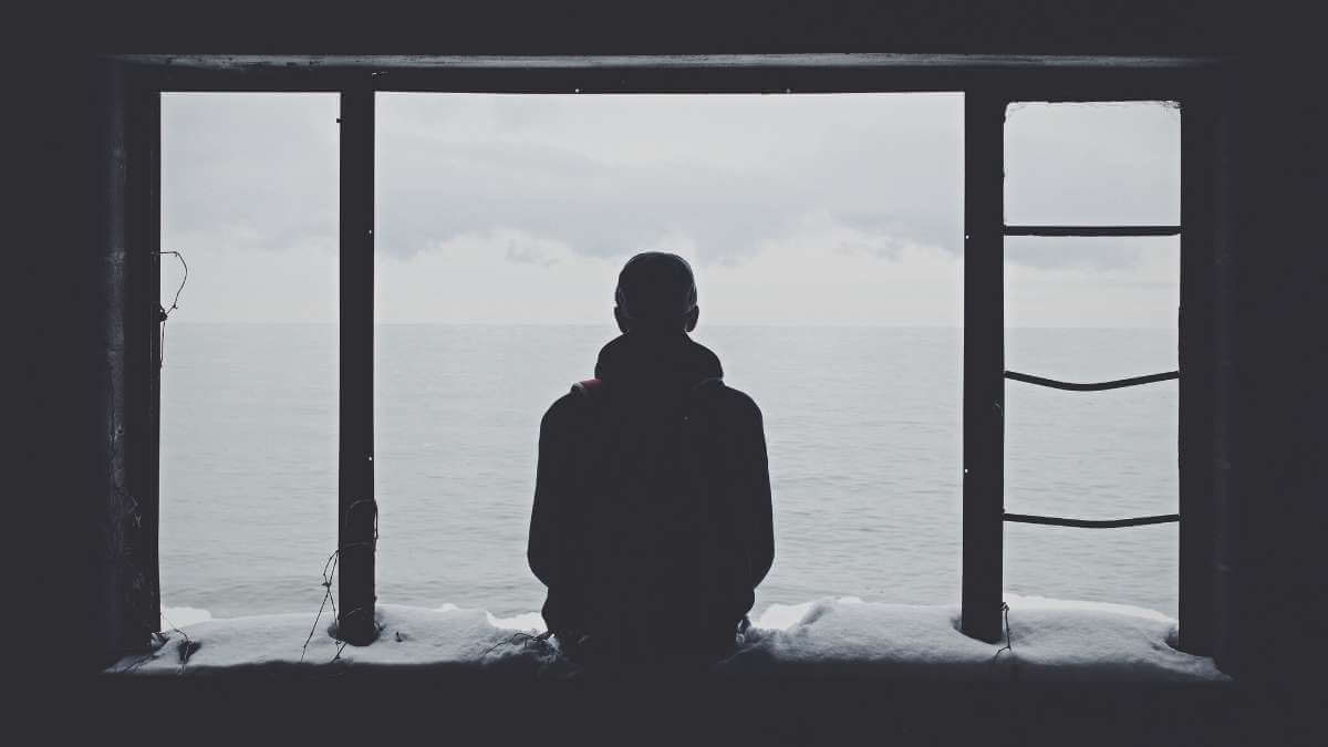 A male escort client sits in a window looking out to sea.