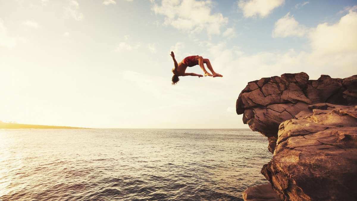A male escort client dives off a rock into the ocean.