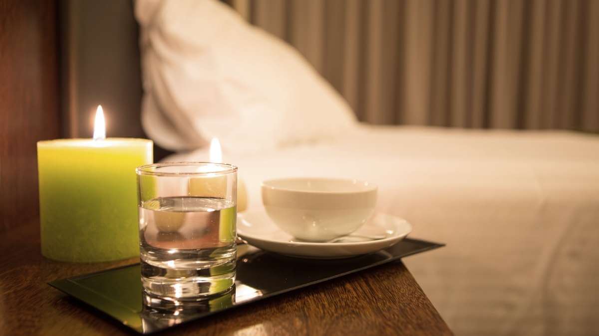 Some cnadles and a glass of water on a hotel room bedside table in an escort incall.