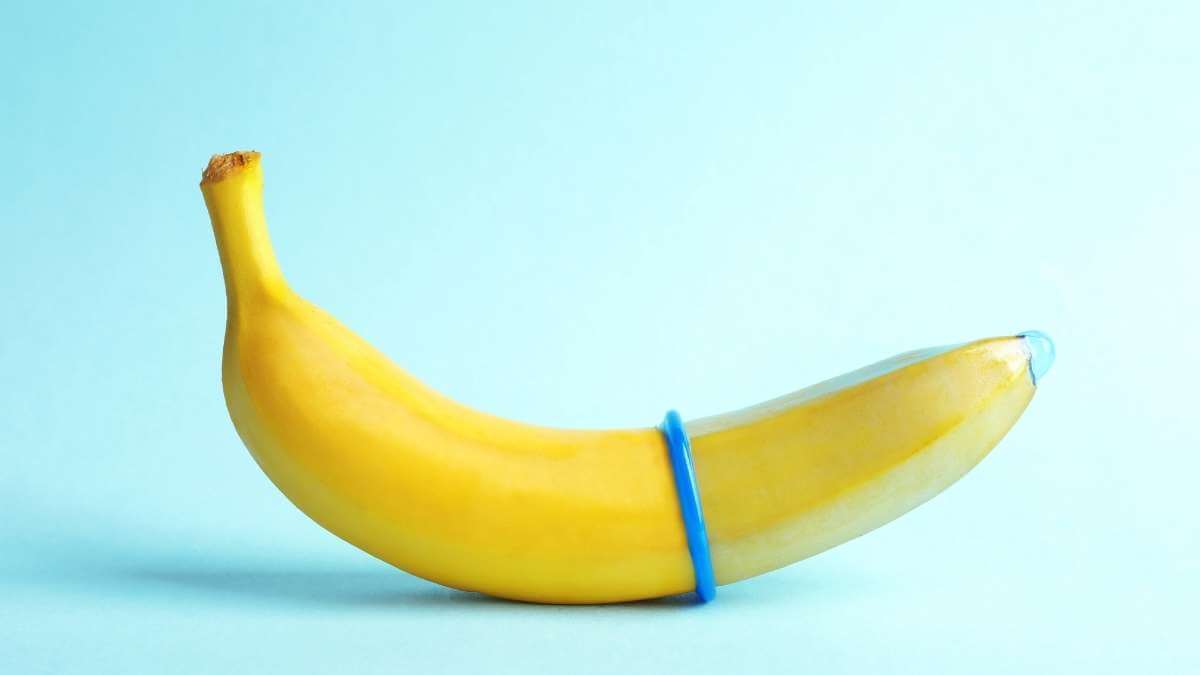 A banana on a blue background with a condom rolled halfway over it.