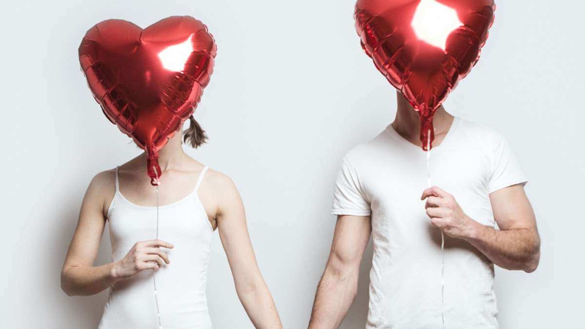 An anonymous female escort and a male escort client hold hands while holding heart-shaped balloons.
