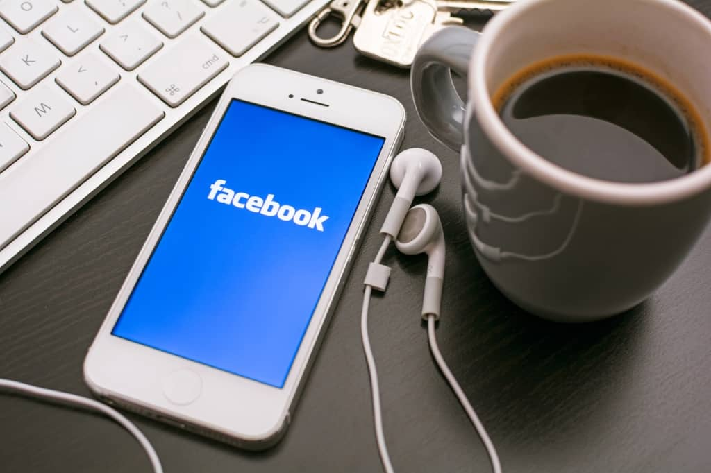 Facebook Statistics - smartphone with Facebook app, ear buds, cup of coffee, keys, laptop