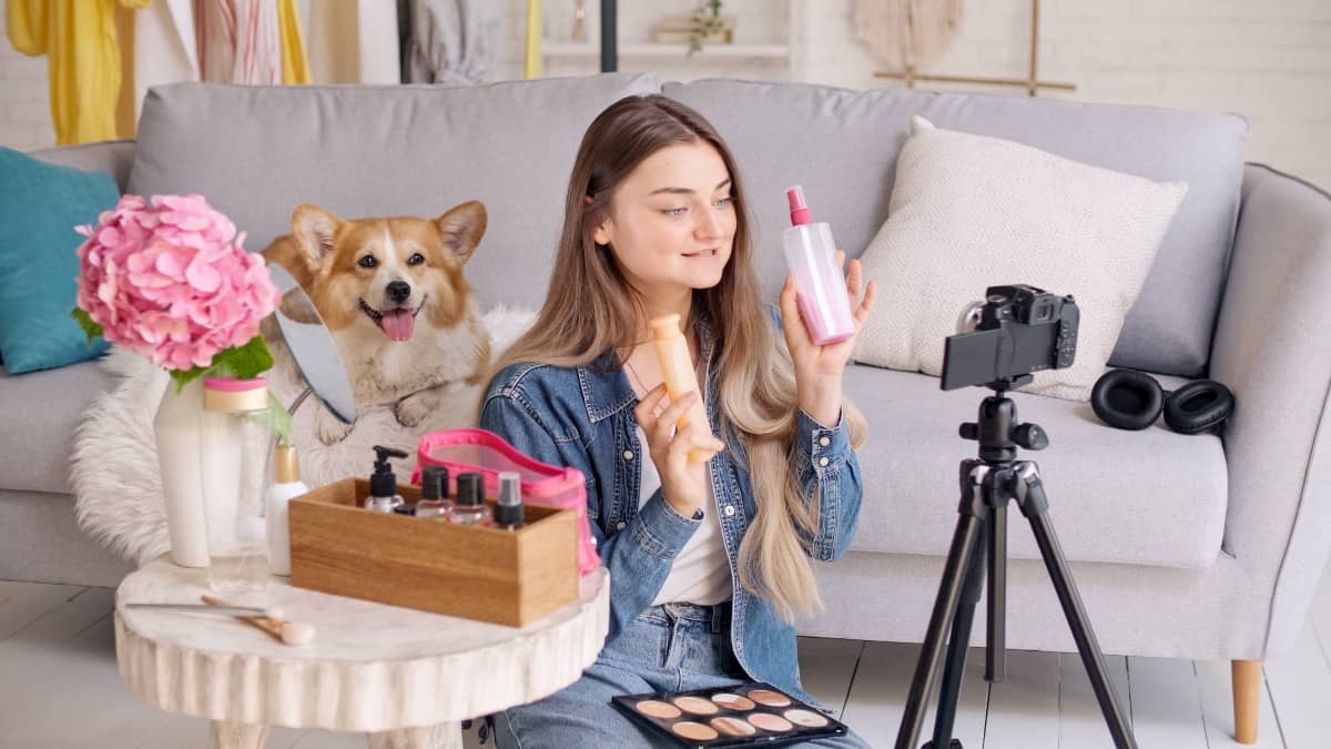 build brand loyalty - young influencer filming herself demonstrating products with a dog sitting on the couch behind her