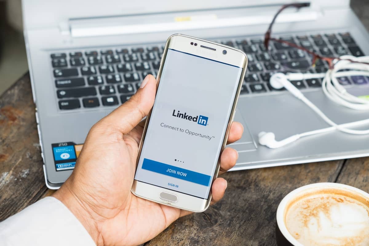 b2b content marketing strategy - picture of smartphone on LinkedIn app with a laptop, coffe, ear buds and glasses in the background