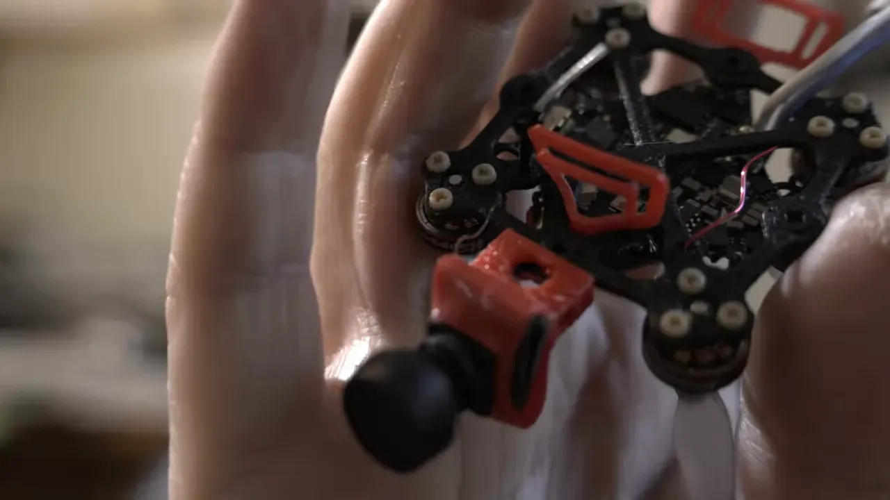 Host holding the tiny 3D printed drone next to a pendant for size comparison