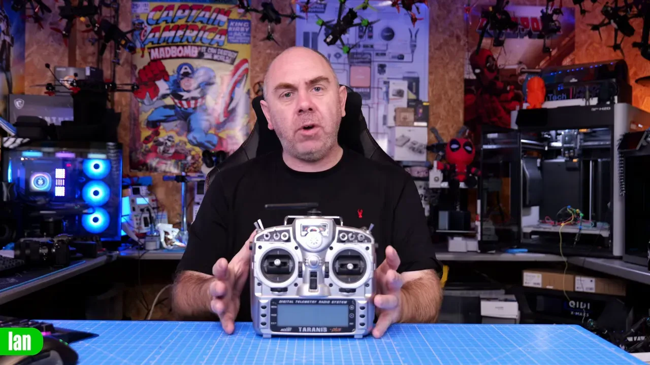 Close front view of FrSky Taranis transmitter on a blue cutting mat with presenter hands framing the radio