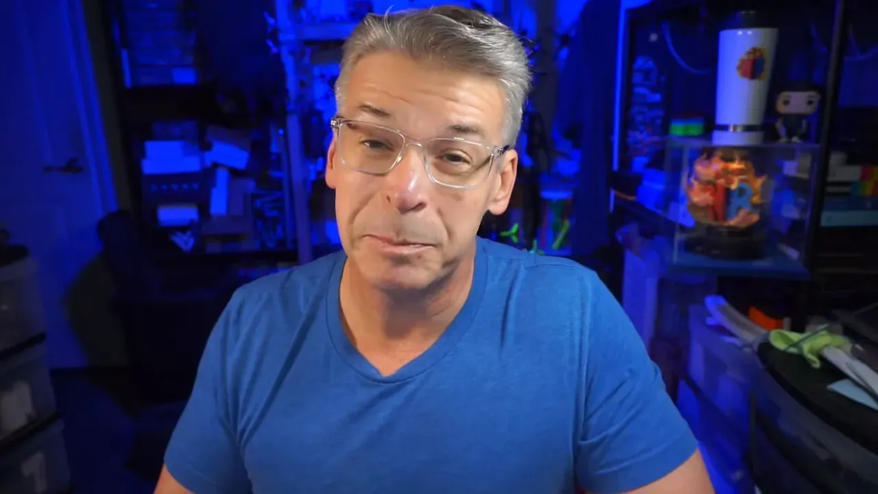 Presenter speaking to camera in a workshop environment with blue lighting, discussing battery longevity