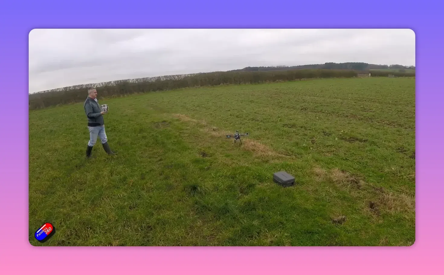 VTOL drone hovering off-target in a field with the operator holding a controller and a case on the ground
