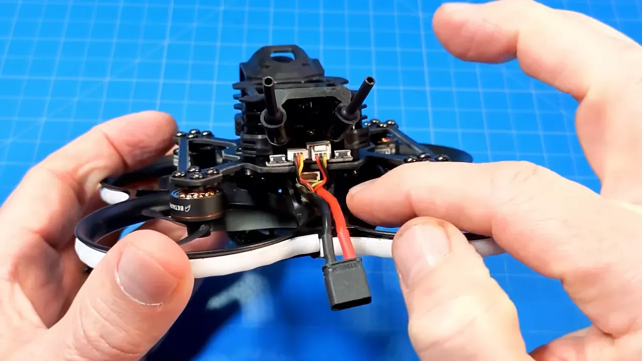 Close-up of Pavo20 Pro II daughter board and battery connector tucked between the camera mount and frame, hands for scale