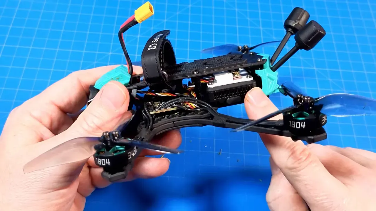 OasisFly35 held in hands showing side profile, tail stack, antennas and tri‑blade props on a blue work mat