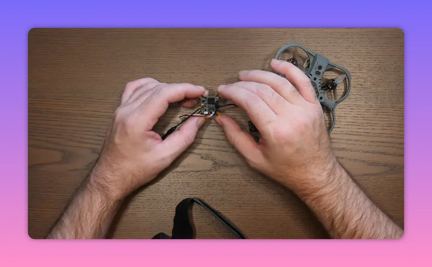Wider top-down image of hands holding a micro VTX/flight board with a ducted micro drone frame visible, showing relative size on the workbench.