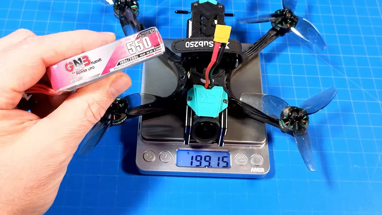 OasisFly35 on a digital scale reading 199.15 g while a hand holds a 550mAh LiPo pack next to the quad for size and weight context.