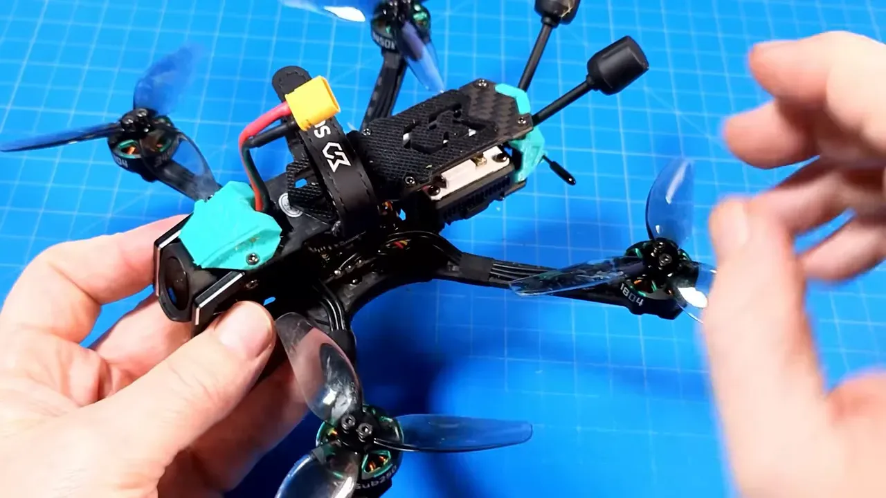 Close shot of OasisFly35 held over a blue cutting mat, showing the camera, arms, props and tidy wiring