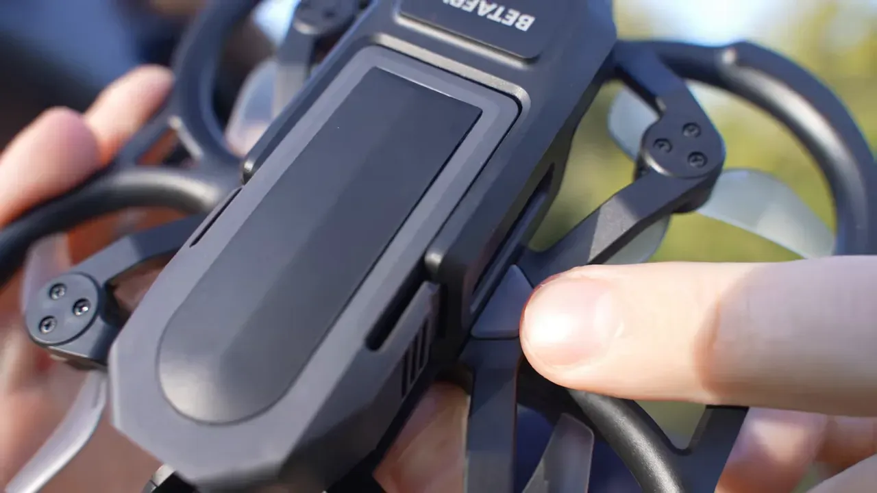 Finger pointing at mode/button on Aquila20 HD micro quad next to prop guard