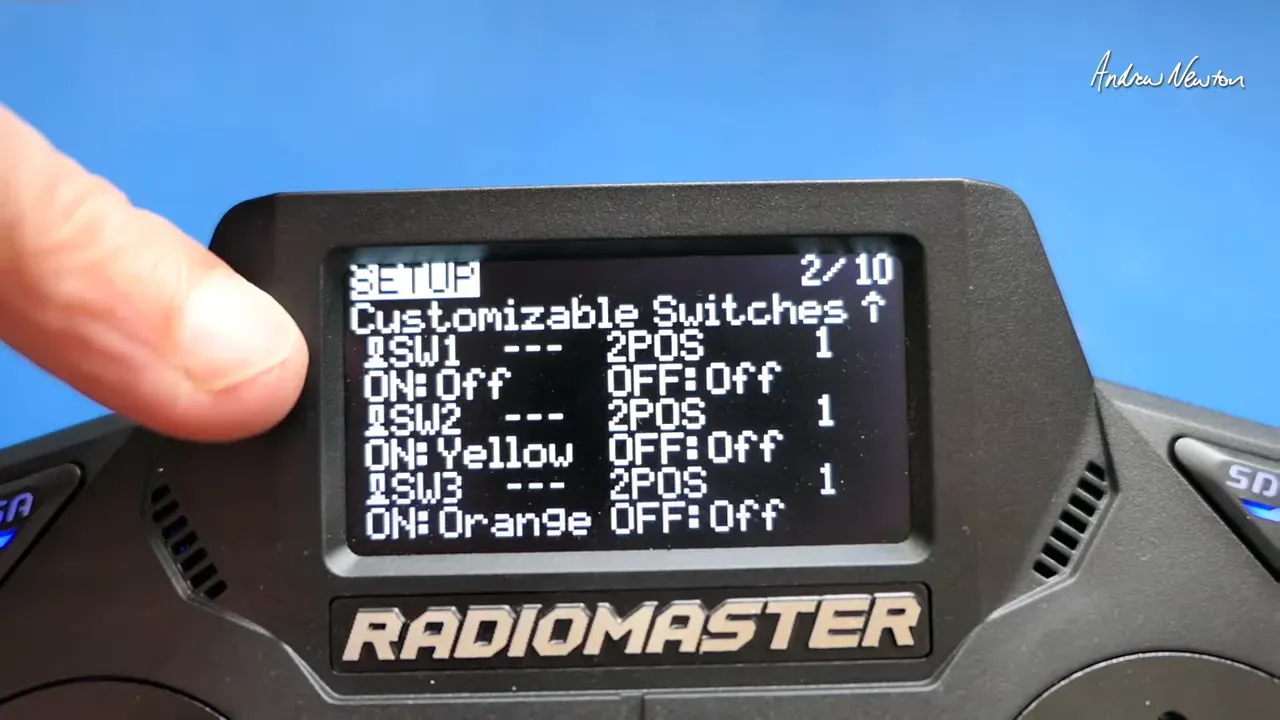 Radiomaster GX12 screen showing the 'Customizable Switches' menu with switch labels, colour names and group numbers, finger pointing at the left edge.