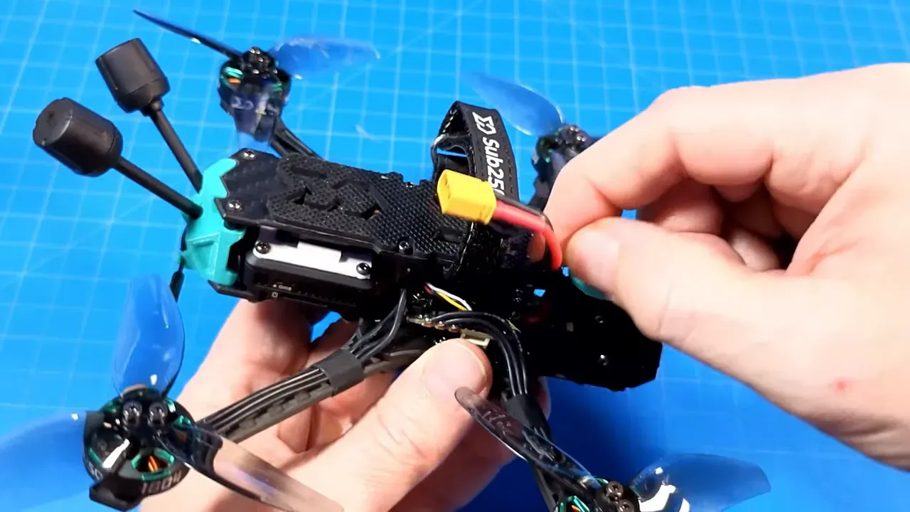 OasisFly35 micro quad with XT60 battery lead being held near the tail stack showing where the power cable exits the flight controller