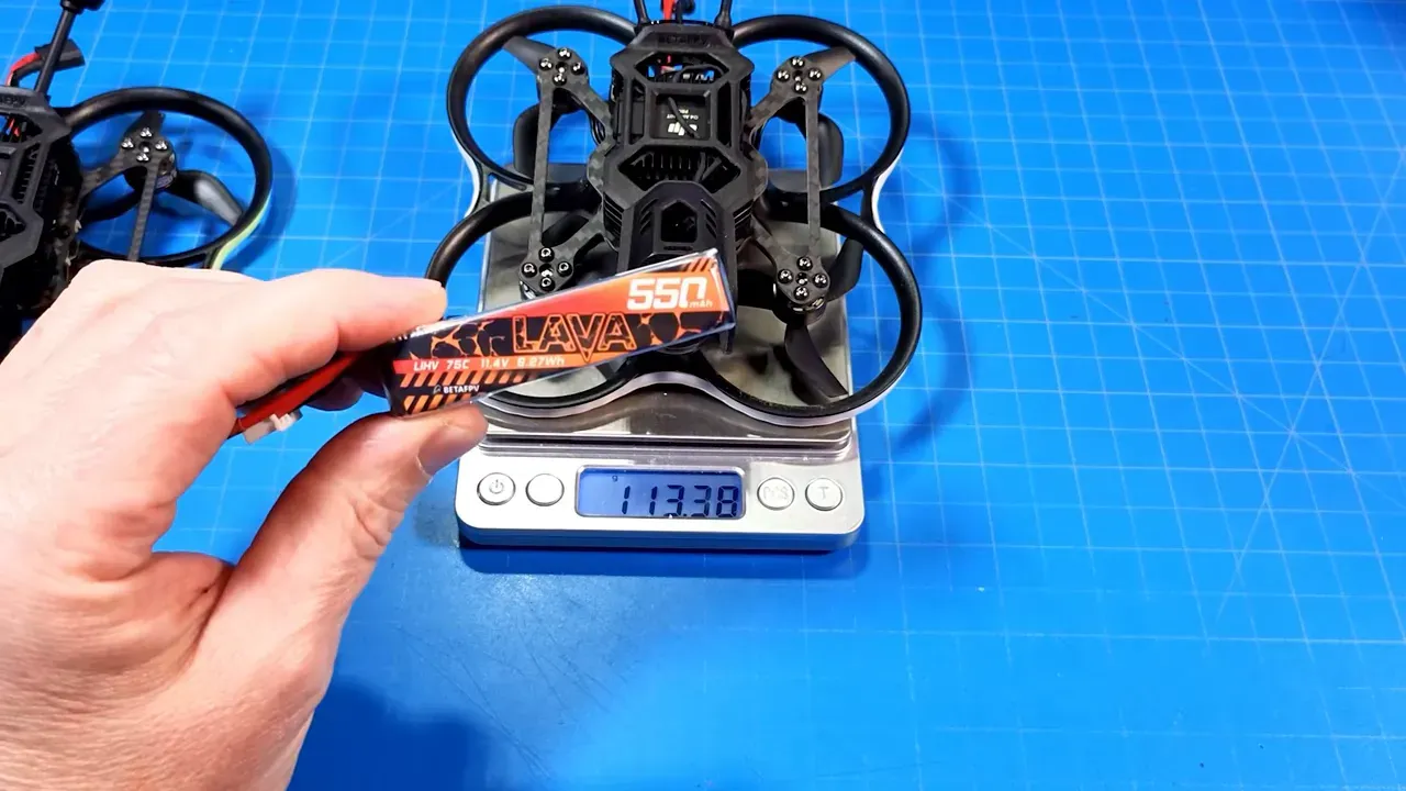 Pavo20 Pro II on a digital scale reading 113.38 grams while a Beta Lava 550 3S battery is held above it