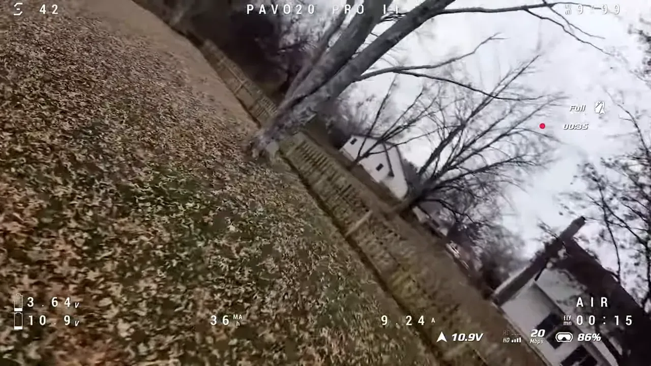 Angled FPV view of a backyard with bare trees, fence and many fallen leaves; PAVO20 PRO II HUD visible indicating flight data