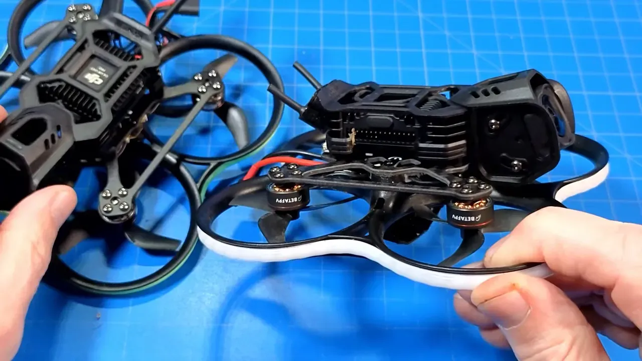 Two Pavo20 micro quads side-by-side on a blue work mat, showing the Pro II in the foreground with antenna and daughterboard details visible