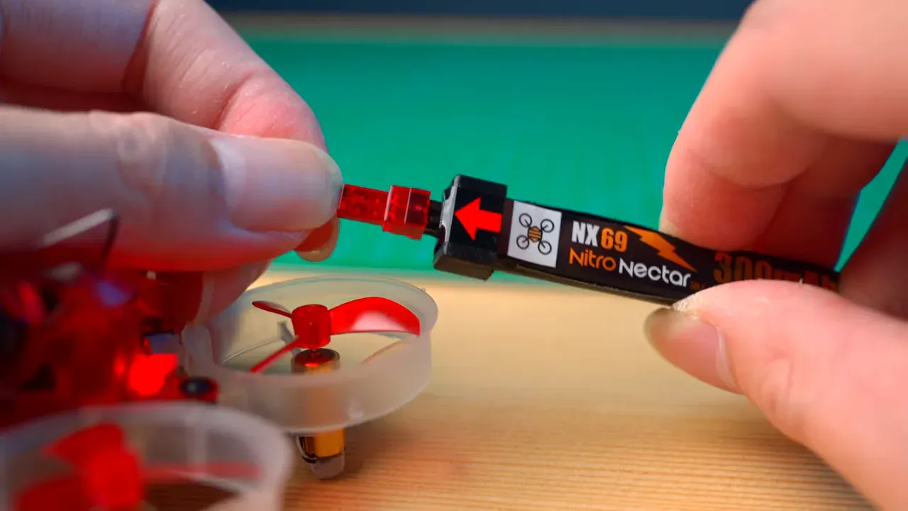 Close-up of a Nitro Nectar NX69 300mAh battery being plugged into a micro whoop — clear view of the NX69 connector and alignment arrow.