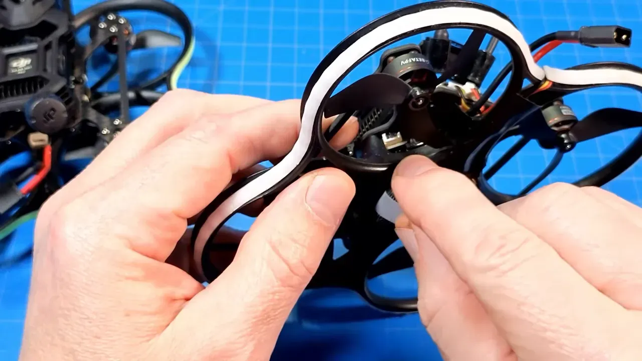 Hands holding a Pavo20 Pro II micro quad showing the daughter board, wiring and camera mount area for scale