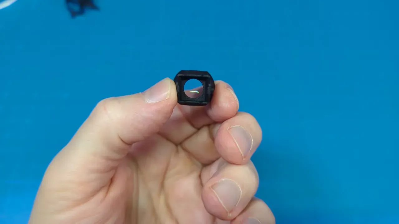 Close-up front view of HappyModel slide-on FOV extender held between fingers showing the lens aperture