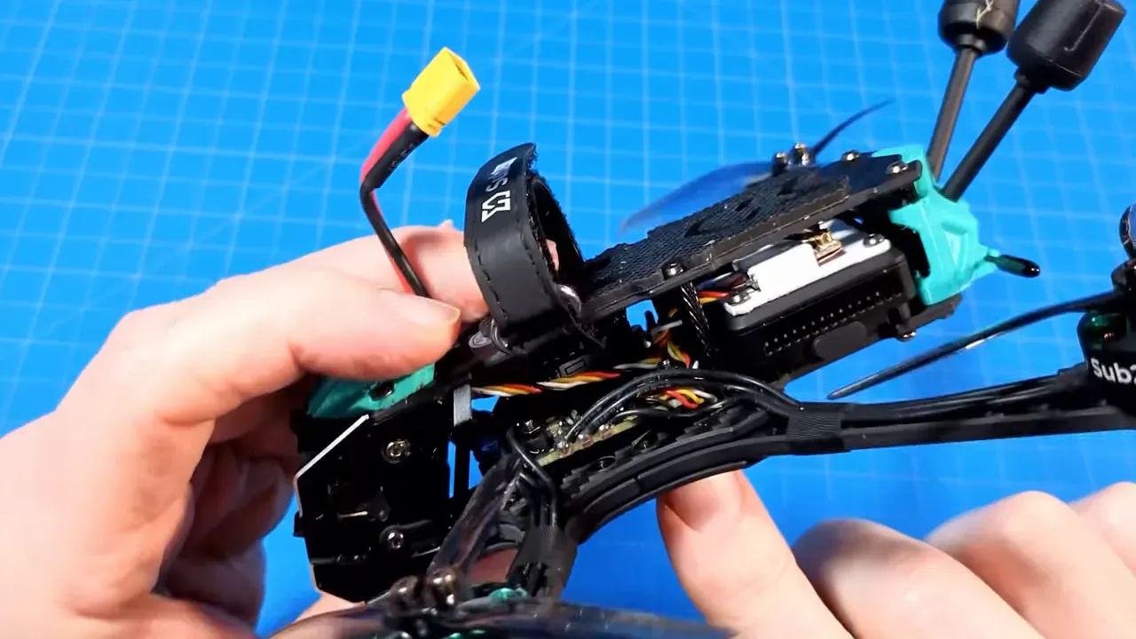 Side close-up of the OasisFly35 showing internal wiring, tail stack, XT30 plug and battery strap while hands hold the frame