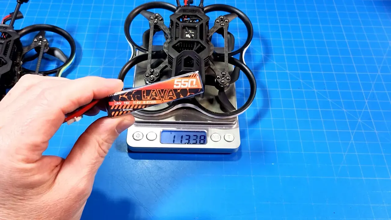 Hand holding a BetaFPV Lava 550 3S battery above a Pavo20 Pro II micro quad on a digital scale