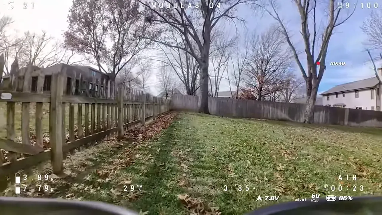 Wide FPV DVR frame of a backyard with a picket fence to the left, trees and houses in the distance and telemetry/O SD visible