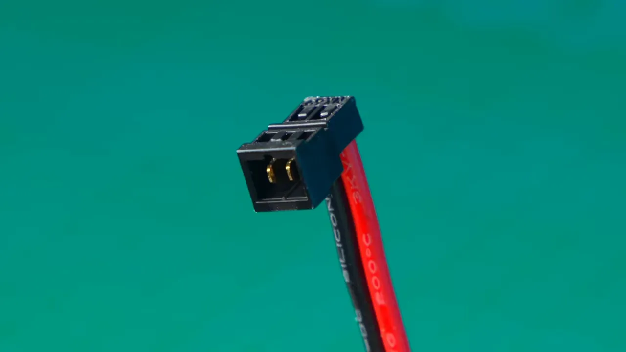 Close-up of the NX69 battery pigtail connector showing the battery-side contact and red/black 20 AWG wires against a green background.