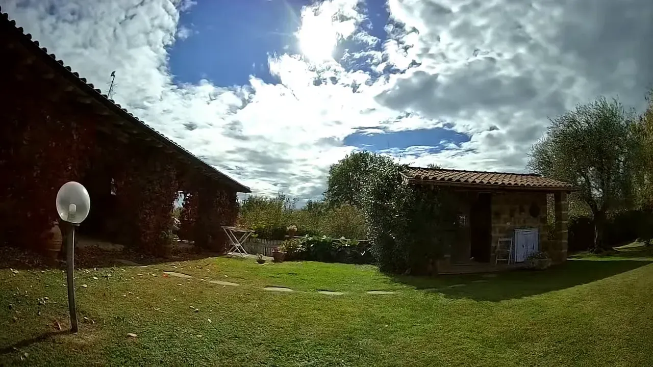 Wide FPV view of a yard with an outbuilding and cloudy sky, lamp post at left and good overall exposure