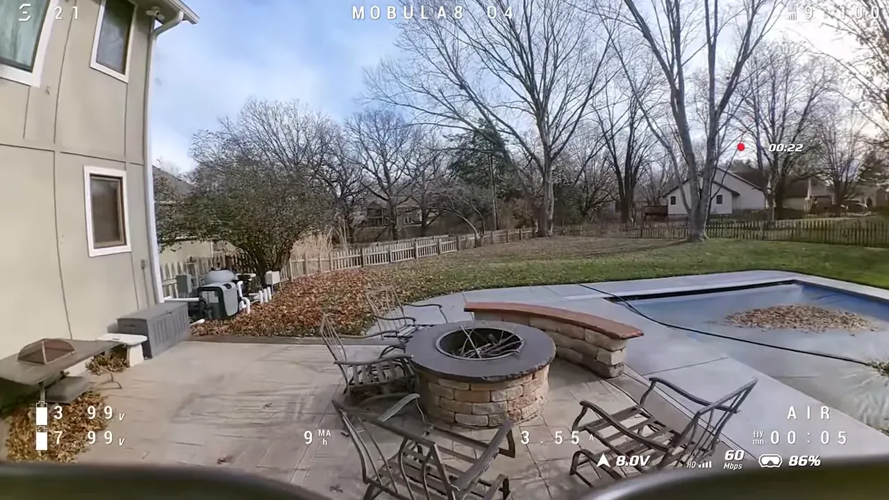 Wider DVR frame of a backyard showing a pool, patio chairs and a fire pit; wide field of view and telemetry visible