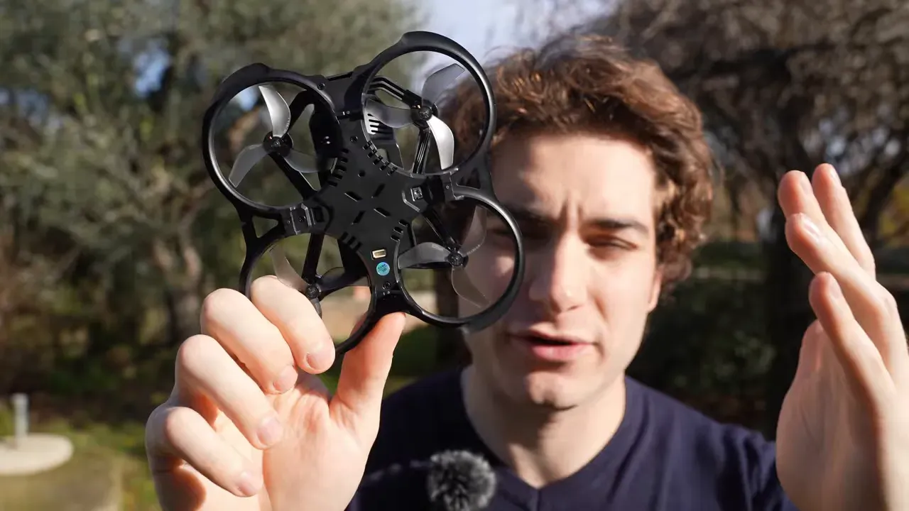 Underside of a BetaFPV Aquila20 HD micro quad showing frame details, vents and sensor housings held by the presenter