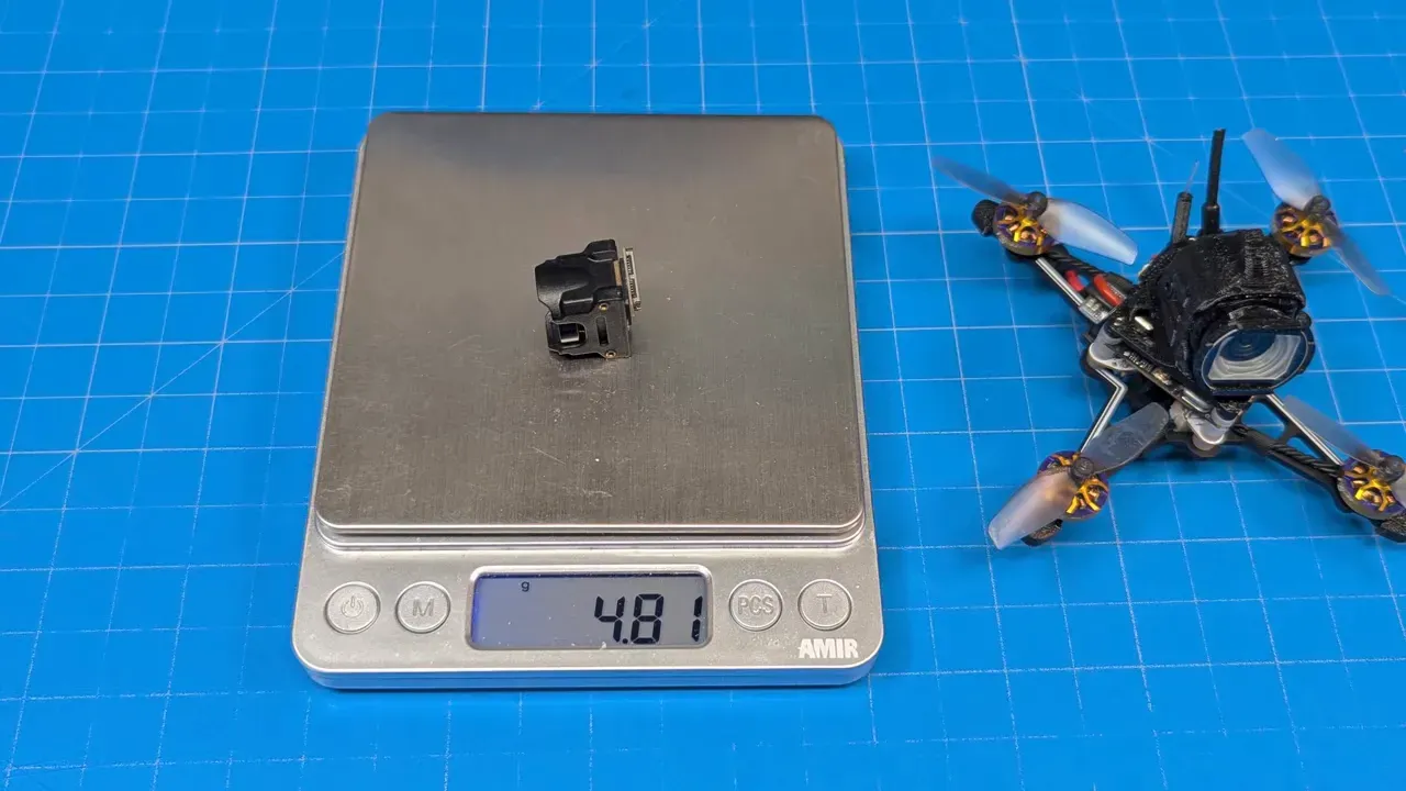 Digital scale reading 4.81 grams with the FlyWoo wide camera module on the scale and a small drone to the right on a blue work mat