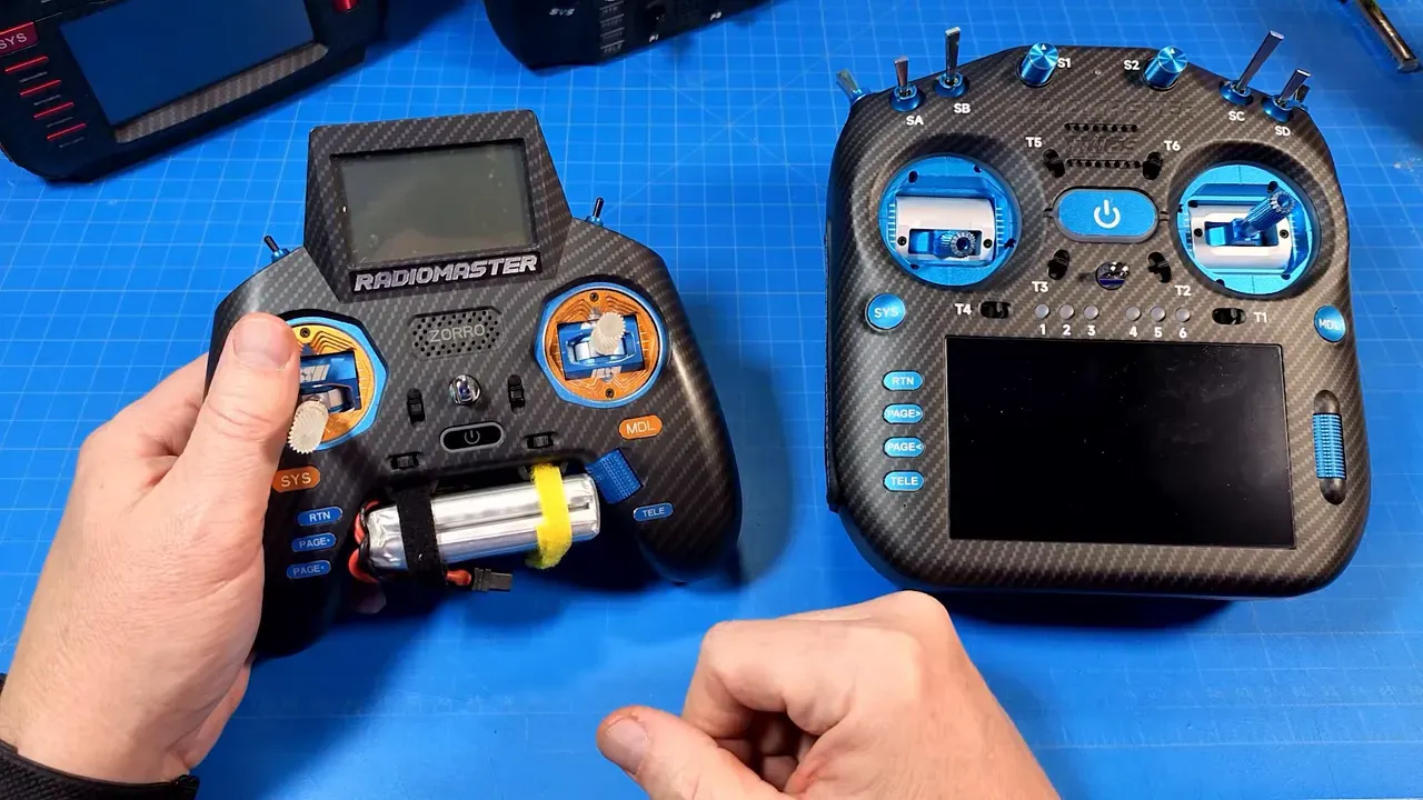 Two transmitters on a blue work mat with hands for scale; RadioMaster TX16S Mk3 Max on the right showing CNC gimbals and stick layout