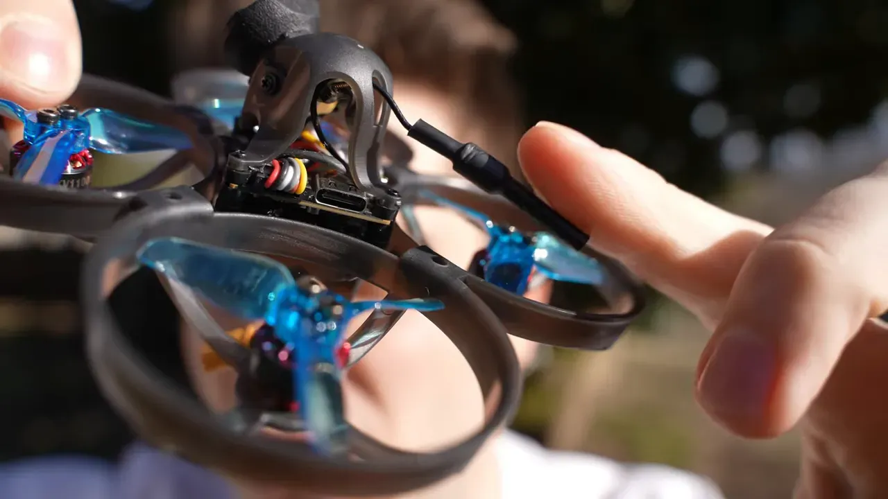 Close-up of the Mobula 8 canopy and antenna plug with a finger pointing at the antenna lead hanging near the prop guard.