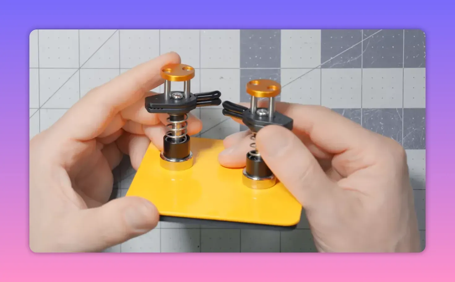 Close-up of a yellow magnetic base with two spring-loaded clips being held and adjusted by hands on a cutting mat