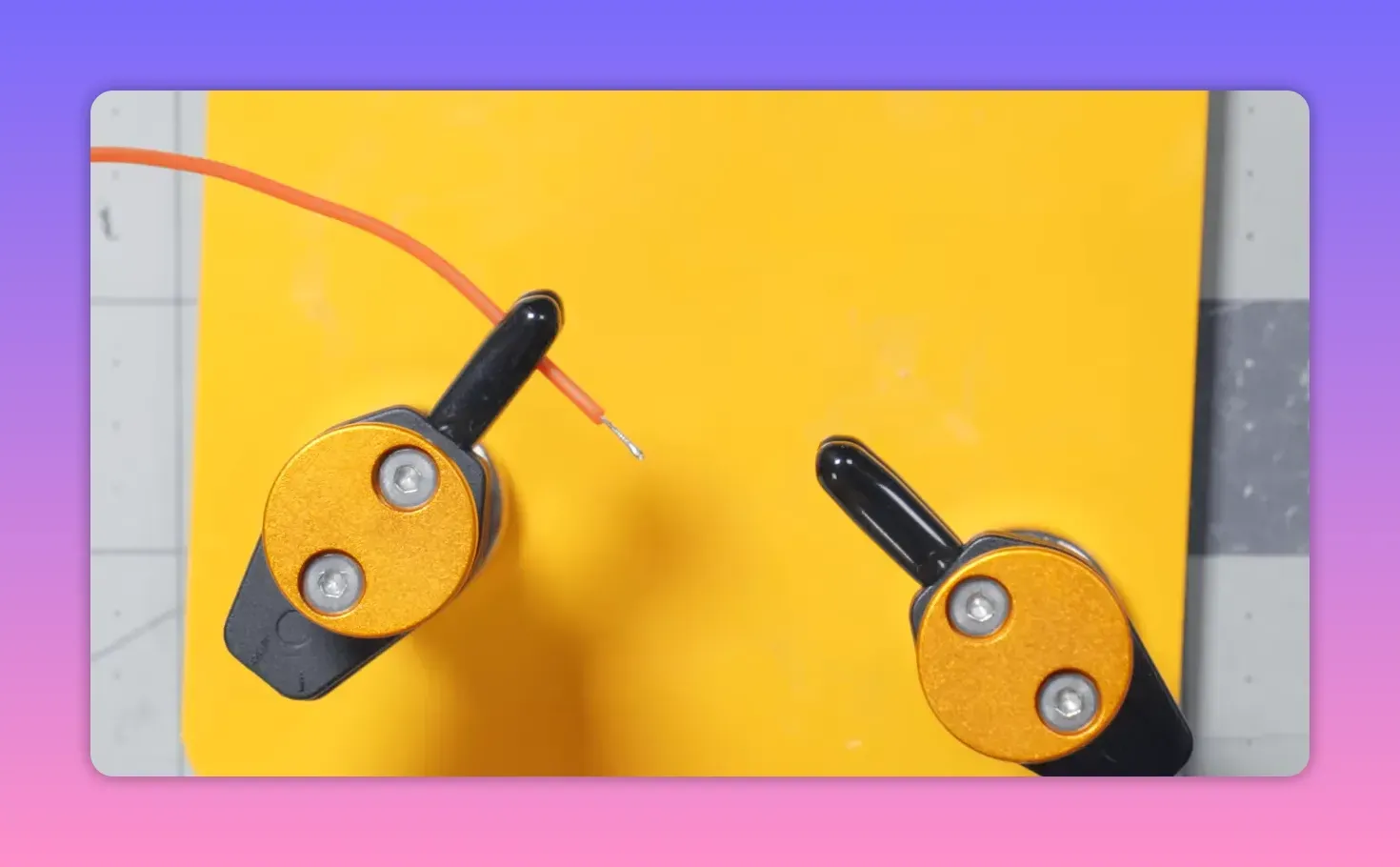 Top-down view of two gold-faced magnetic clips on a yellow background holding stripped orange wire ends, showing how the clips grip the wire