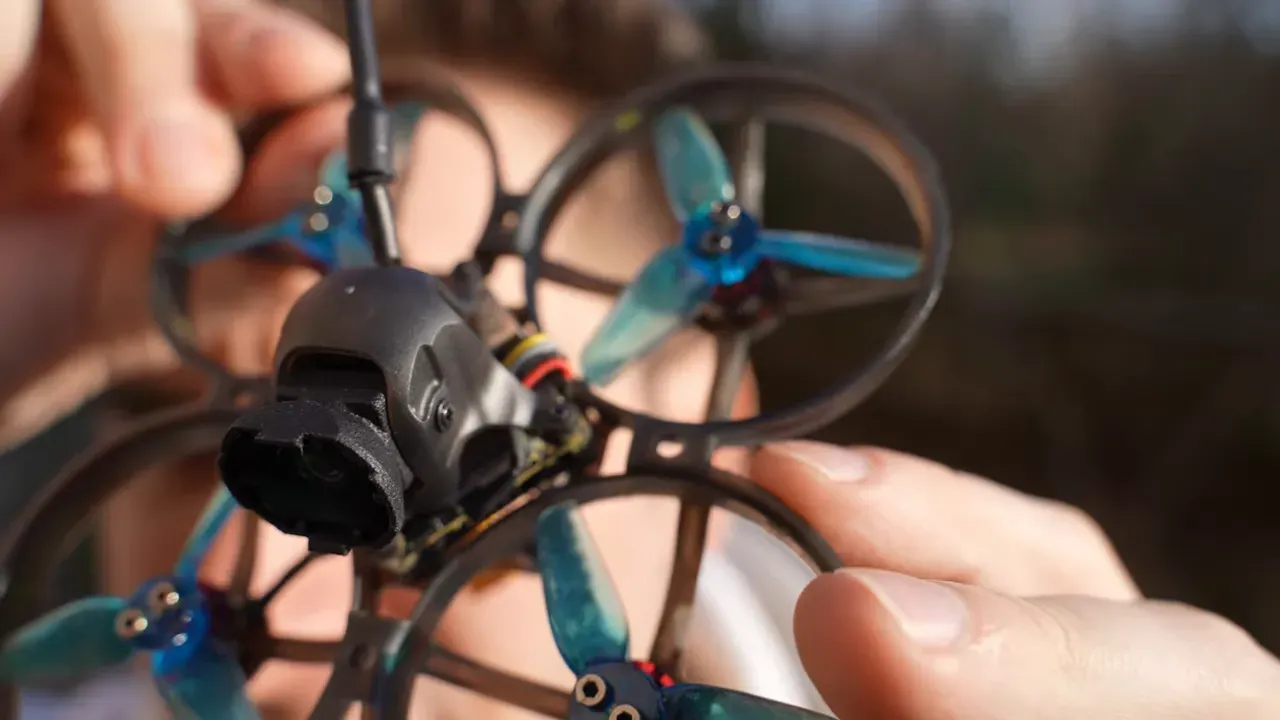 Hand-held Mobula 8 front close-up showing O4 Lite camera, canopy and antenna plug with finger for scale