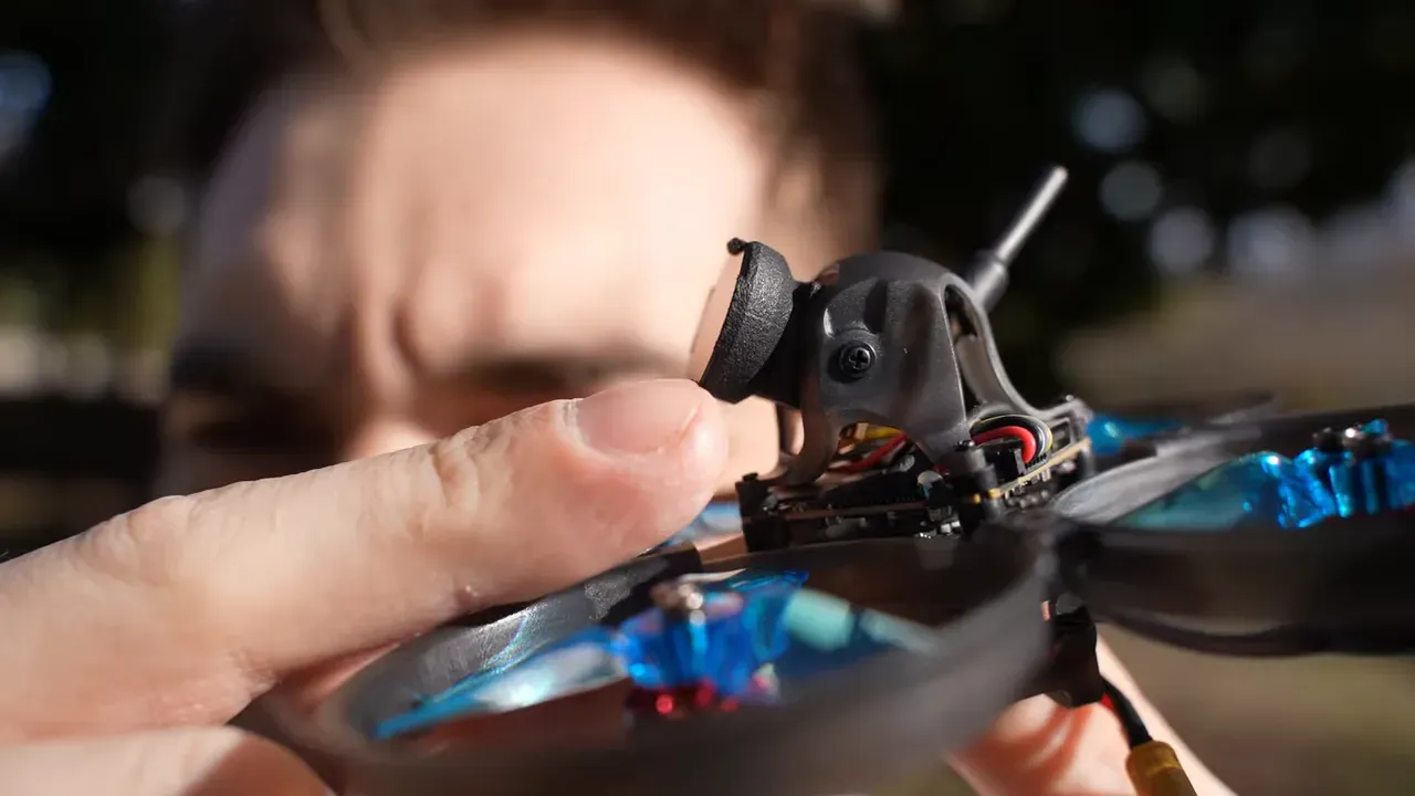 Tight close-up of the Mobula 8 O4 Lite camera with the wide-angle/filter adapter mounted and a finger pointing at the adapter