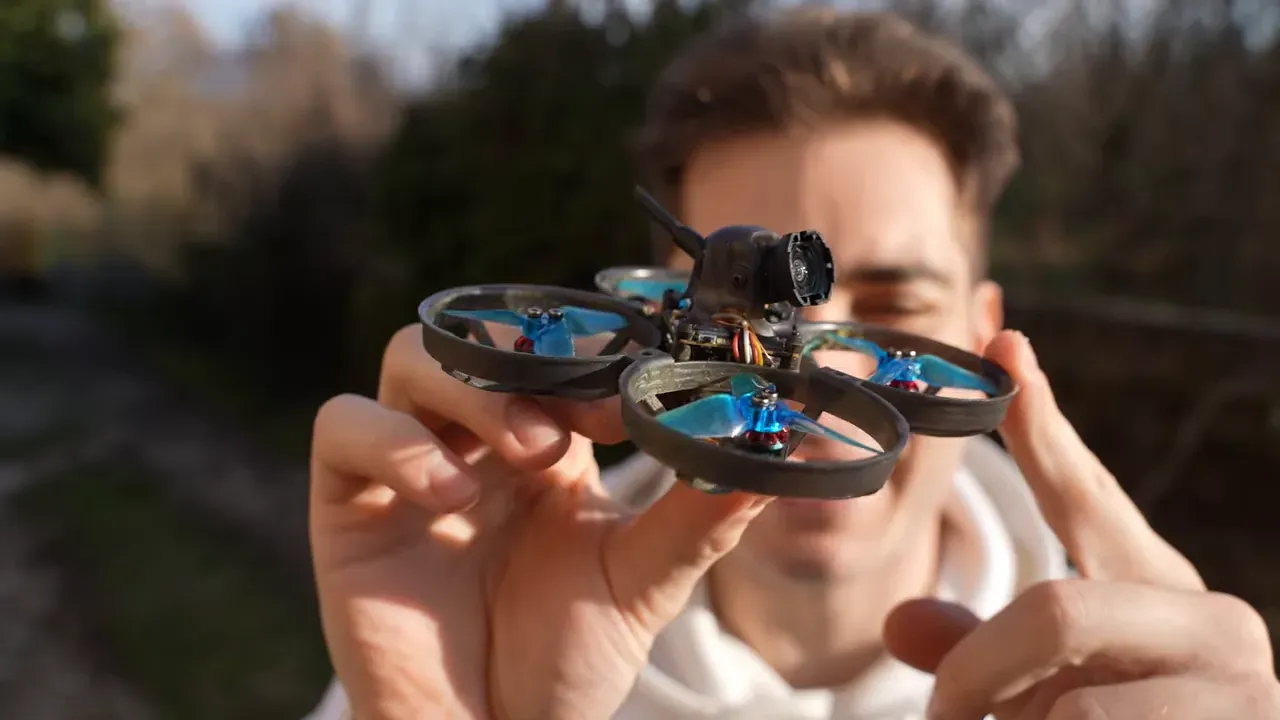 Close-up of the Mobula 8 tiny whoop held in front of the reviewer showing the O4 Lite camera, swiveling mount and ducted props