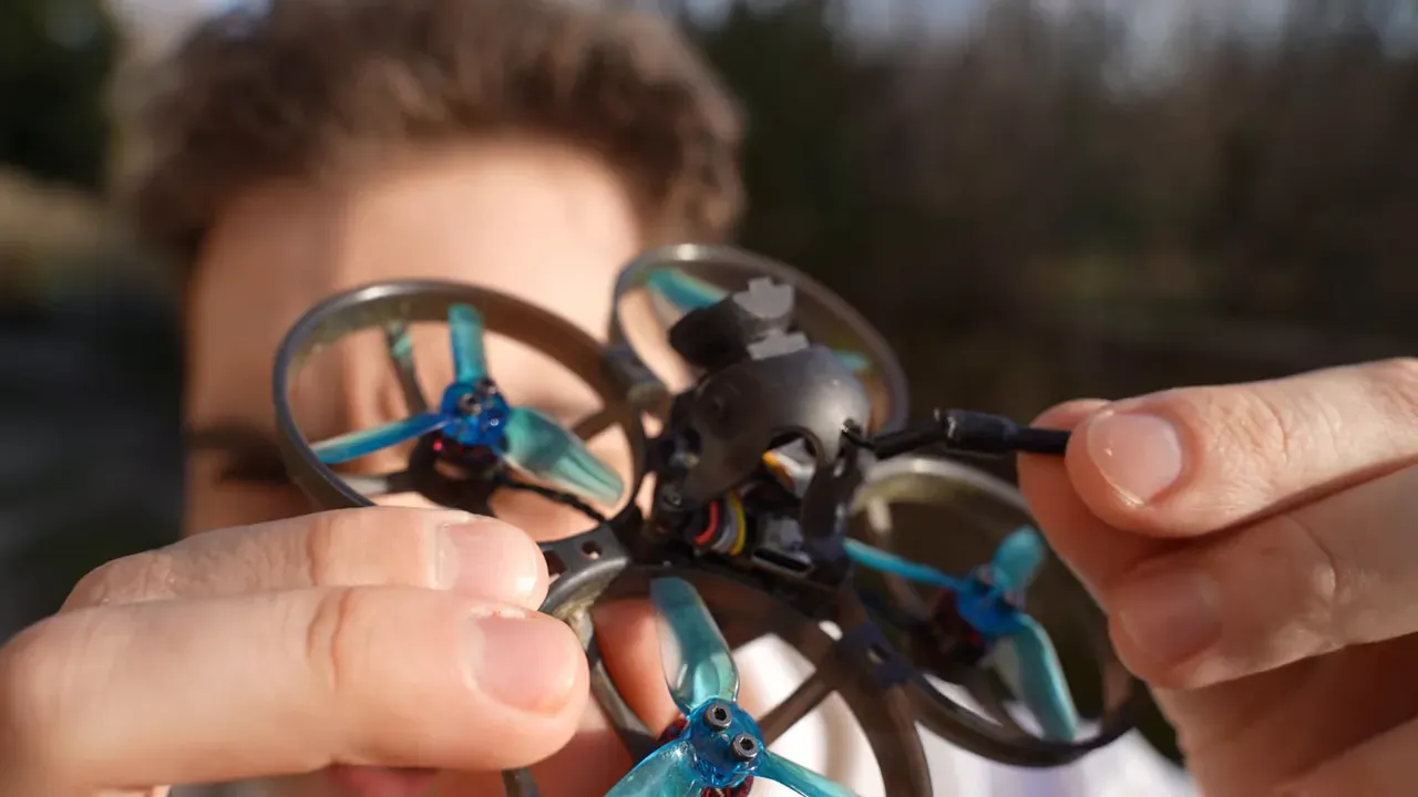 Close-up of the Mobula 8 showing the canopy and antenna plug dangling while the reviewer holds the drone