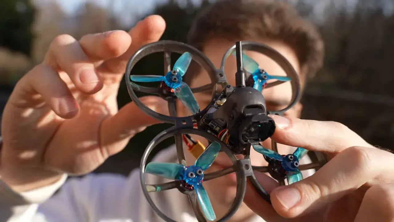 Close-up of the Mobula 8 tiny whoop held up to camera showing the O4 Lite camera, front mount and ducted prop guards