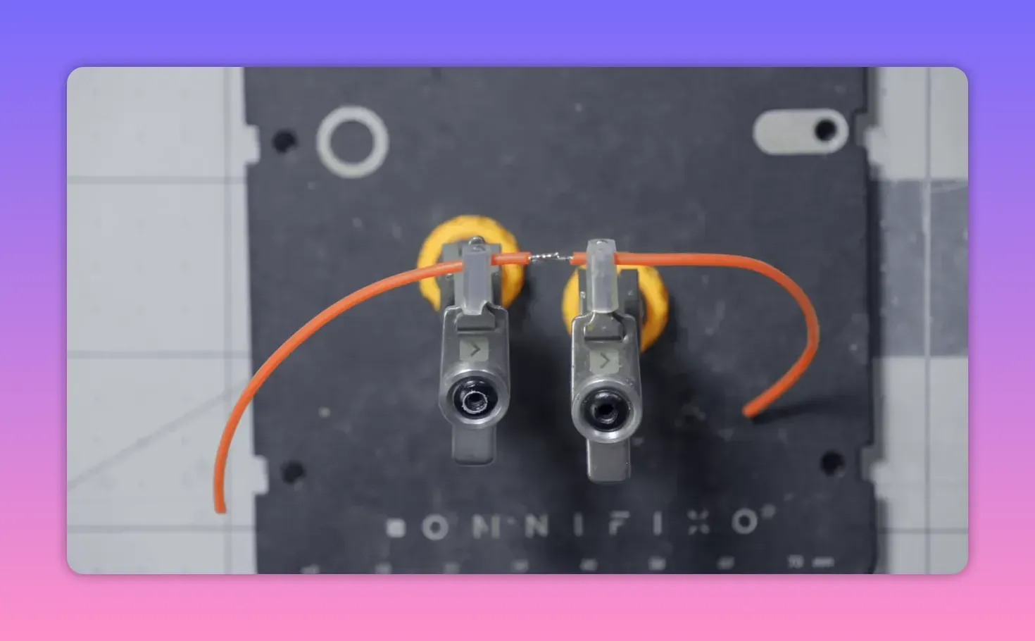 Overhead shot of two metal clips mounted on a black magnetic base holding orange wires aligned with a small tinned splice between them