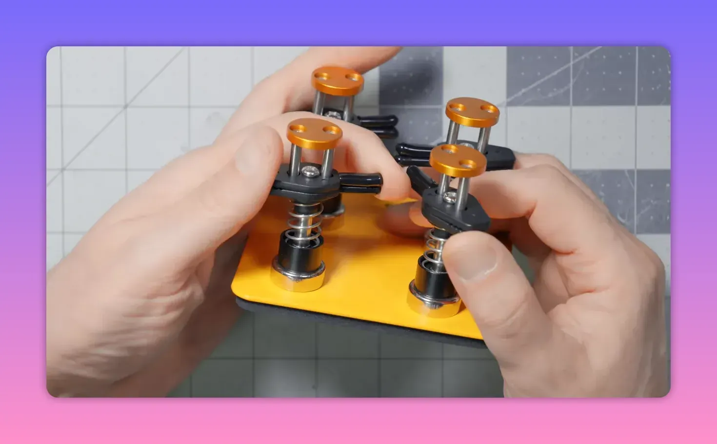 Top-down view of hands adjusting a yellow magnetic two-clip helping-hands base with orange caps and visible springs, on a cutting mat
