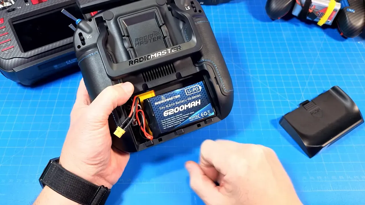 Clear view of RadioMaster TX16S Mk3 Max with 6200mAh battery pack installed in rear compartment and battery cover removed on a blue work mat