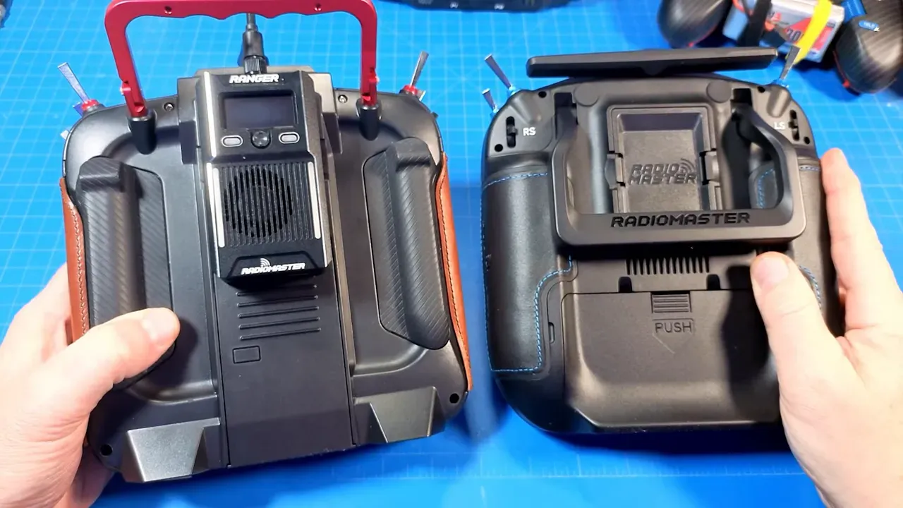 Bench comparison of two transmitters showing a metal handle on the left and the Radiomaster plastic rear handle on the right with hands for scale