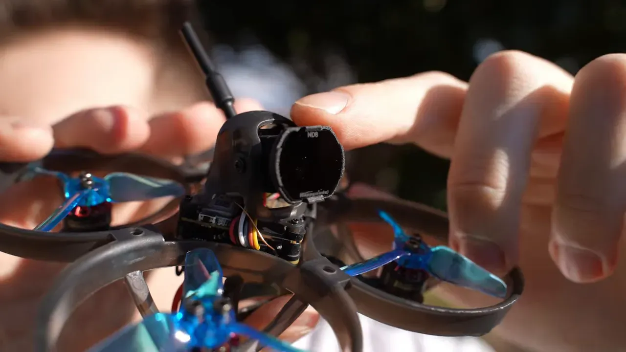 Close-up of the Mobula 8 showing the O4 Lite camera with ND filter and the molded camera mount while fingers adjust it